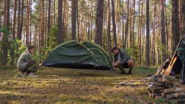 Beyaz adam ve kadın birlikte çalışarak, güzel bir çam ormanında yeşil bir turist çadırı kurarak, kamp yerlerini gece boyunca açık hava maceralarının tadını çıkararak hazırlıyorlar.