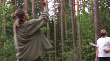 Güzel bir çam ormanında badminton oynayan genç atletik çift yaz tatillerinde dışarıda eğleniyor ve aktif ve sağlıklı bir yaşam tarzı sergiliyor.