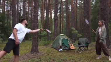 Mutlu çift güzel bir çam ormanında badminton oynayarak, bir çadır ile kamp yaparken ve yaz tatili boyunca doğada dinlenirken dışarıda eğlenerek vakit geçiriyor.