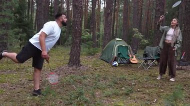 Mutlu çift güzel bir çam ormanında badminton oynayarak, bir çadır ile kamp yaparken ve yaz tatili boyunca doğada dinlenirken dışarıda eğlenerek vakit geçiriyor.
