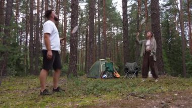 Mutlu çift güzel bir çam ormanında badminton oynayarak, bir çadır ile kamp yaparken ve yaz tatili boyunca doğada dinlenirken dışarıda eğlenerek vakit geçiriyor.