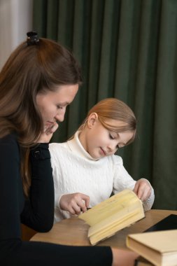 Anne, evde birlikte kitap okurken genç kızına sabırla kavramları anlatıyor, eğitim ve aile bağlarına odaklı destekleyici bir öğrenme ortamı yaratıyor. Dikey fotoğraf