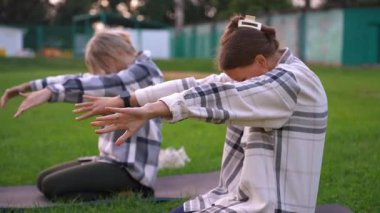 İki rahat kadın parkta yoga minderlerinde otururken nefes egzersizleri ve asma yapıyorlar. Sağlıklı yaşam tarzı meraklıları açık hava egzersizleri sırasında farkındalık ve meditasyon pratiği yapıyorlar.