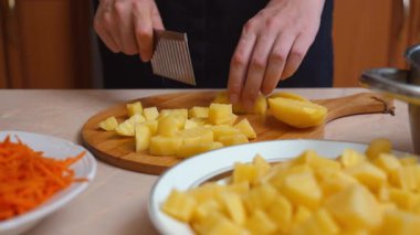 Profesyonel aşçı ahşap bir tahta üzerinde kırışıklık kesici ile haşlanmış patatesleri küçük küplere dikkatlice kesiyor. Bu hazırlık yemek için geleneksel sebze salatası yapmak için bir adımdır.