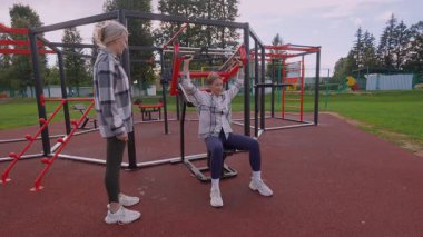 Spor salonunda kollarını ve omuzlarını egzersiz makinesinde çalıştıran genç bir kadın. Kadın özel antrenörü spor sırasında motivasyon ve destek sağlıyor.