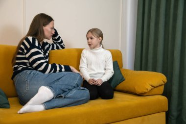 Anne ve kız evdeki sarı kanepede ciddi ciddi konuşuyor, sorunları tartışıyor ve önemli aile sorunları hakkında iletişim kuruyor, ebeveynlik ve çocuk gelişimine odaklanıyor