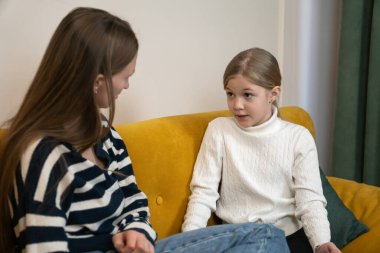 Parlak sarı bir kanepede oturan iki kız kardeş önemli aile meseleleri hakkında ciddi ve destekleyici bir tartışmaya giriştiler.