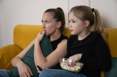 Genç anne ve kızı evdeki rahat bir kanepede oturup patlamış mısırlarını paylaşıyorlar ve heyecanlı bir şekilde oturma odasındaki film gecesinde birlikte vakit geçirip eğleniyorlar.