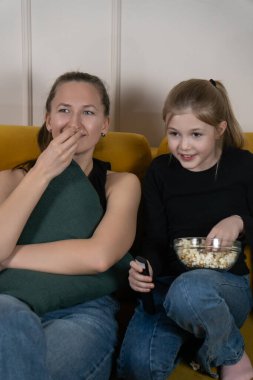 Anne ve kızı oturma odalarındaki sarı bir kanepede gevşeyip patlamış mısır yiyip uzaktan kumanda tutarak sıradan bir film gecesinin tadını çıkarıyorlar. Dikey fotoğraf