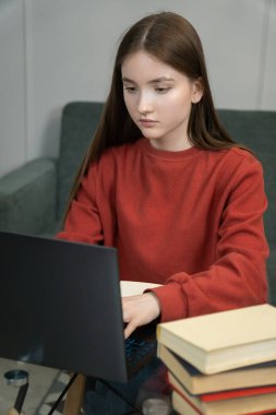 Genç kız dizüstü bilgisayar kullanırken, not alırken ve evde çalışırken, çevrimiçi öğrenme, uzaktan çalışma ya da eğitim kavramını gösterirken konsantre oluyor. Dikey fotoğraf