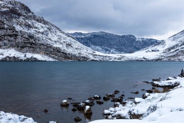 Enol Gölü 'nün karanlık suları güneş doğmadan önce sabah erken saatlerde karla kaplı dağlarla çevrili. Covadonga Gölleri, Picos de Europa, Asturias, İspanya.
