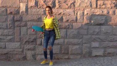 Genç bir kadın elinde kaykayla dans ediyor.