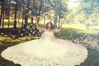 Gül yapraklarıyla çimlerin üzerinde oturan gelin. Mutlu gelin ve düğün konsepti