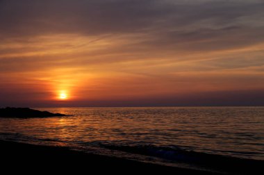 Gün batımında deniz üzerinde renkli gökyüzü olan kumlu sahilin manzarası.