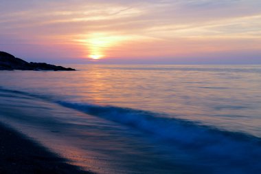 Gün batımında deniz üzerinde renkli gökyüzü olan kumlu sahilin manzarası.