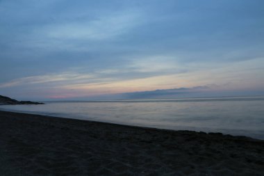 Gün batımında deniz üzerinde renkli gökyüzü olan kumlu sahilin manzarası.