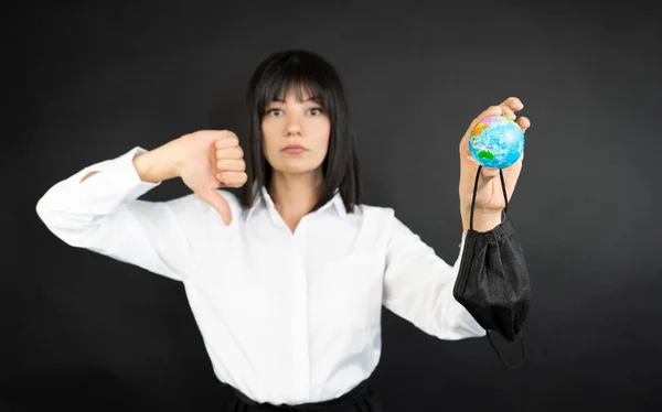 İş kadını siyah arka planda duruyor ve elinde küçük bir dünya var. 