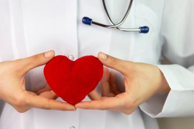 Kadın doktorların elleri kırmızı kalbi tutuyor ve steteskopun kafasını yakınlaştırıyor. Tıbbi yardım ya da sigorta konsepti. Kardiyoloji ve sağlık. Kalp ameliyatı ve canlandırma konsepti