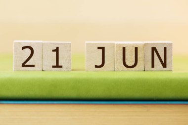 Wooden cubes calendar for 21 JUNE on green book, closeup