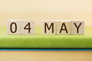 Wooden cubes calendar for 04 MAY on green book, closeup