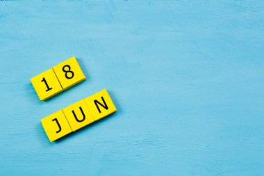 Mavi ahşap yüzeyde, 18 Haziran 'lı sarı küpler takvimi ve kopyalama alanı