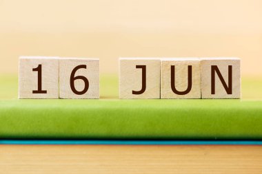 Wooden cubes calendar for 16 JUNE on green book, closeup