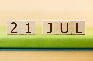 Wooden cubes calendar for 21 JULY on green book, closeup