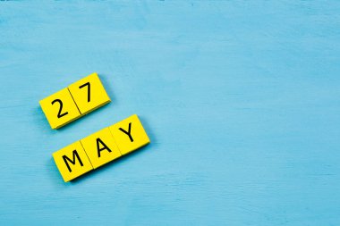 Mavi ahşap yüzeyde 27 MAY ve kopyalama alanı olan sarı küpler takvimi