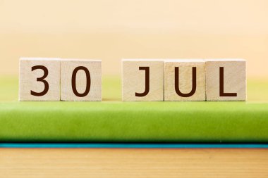Wooden cubes calendar for 30 JULY on green book, closeup