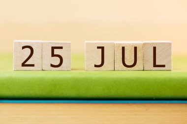 Wooden cubes calendar for 25 JULY on green book, closeup