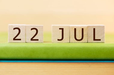 Wooden cubes calendar for 22 JULY on green book, closeup