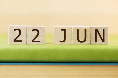 Wooden cubes calendar for 22 JUNE on green book, closeup