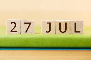 Wooden cubes calendar for 27 JULY on green book, closeup