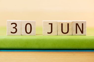 Wooden cubes calendar for 30 JUNE on green book, closeup
