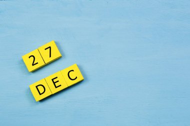 Mavi ahşap yüzeyde, 27 Aralık tarihli sarı küpler takvimi ve kopyalama alanı