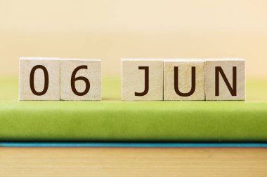 Wooden cubes calendar for 06 JUNE on green book, closeup