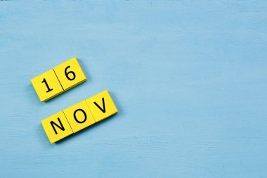 Mavi ahşap yüzeyde, 16 Kasım tarihli sarı küpler takvimi ve kopyalama alanı