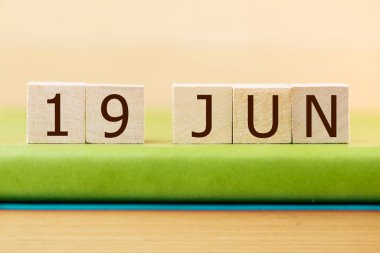 Wooden cubes calendar for 19 JUNE on green book, closeup