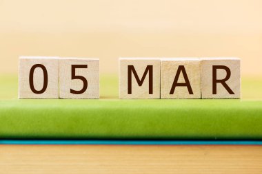 Wooden cubes calendar for 05 MARCH on green book, closeup