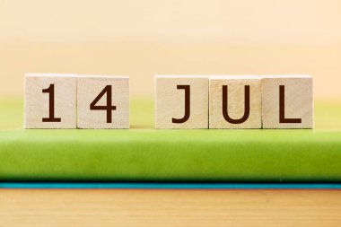 Wooden cubes calendar for 14 JULY on green book, closeup