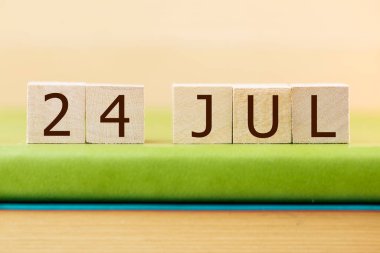 Wooden cubes calendar for 24 JULY on green book, closeup