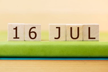 Wooden cubes calendar for 16 JULY on green book, closeup