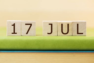 Wooden cubes calendar for 17 JULY on green book, closeup