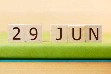 Wooden cubes calendar for 29 JUNE on green book, closeup