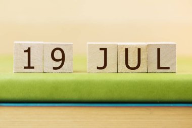 Wooden cubes calendar for 19 JULY on green book, closeup