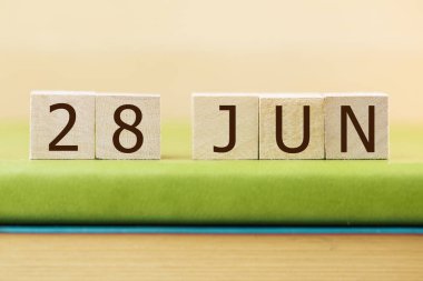 Wooden cubes calendar for 28 JUNE on green book, closeup