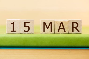 Wooden cubes calendar for 15 MARCH on green book, closeup
