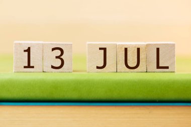 Wooden cubes calendar for 13 JULY on green book, closeup