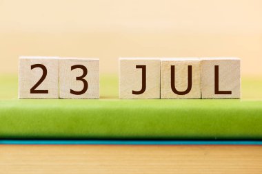 Wooden cubes calendar for JULY 23 on green book, closeup