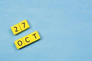 Mavi ahşap yüzeyde, 27 Ekim tarihli sarı küpler takvimi ve kopyalama alanı